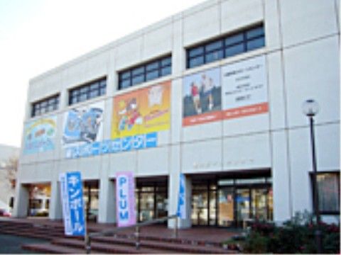 レンガの低めの階段が数段上がったところに、1階がガラス張りで白い外壁の2階以上ある建物が建っている。玄関へ続く手すりにのぼりがある。