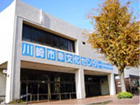 レンガ調の道に大き目な樹木が立っており、その前に四角い2階建ての公共施設がある。外壁に大きく名称が書かれている。