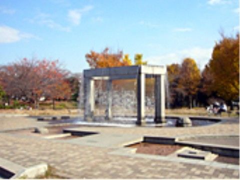 公園のタイル張りの広場の中央に噴水と一体となった石張りの四角いモニュメントがある。周囲には浅めの水路がある。