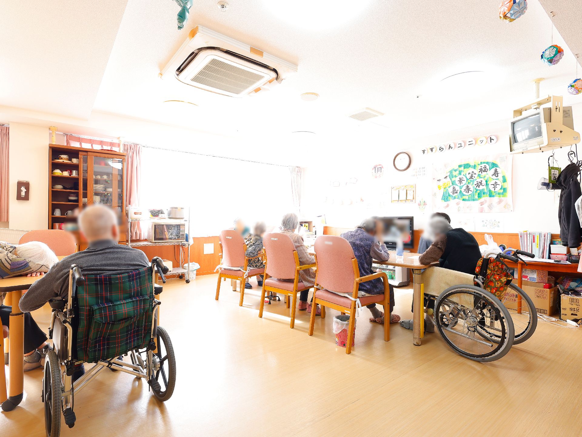 屋外で男性スタッフが車いすを押し、高齢女性が車いすに座り、誰かに手を振っている。