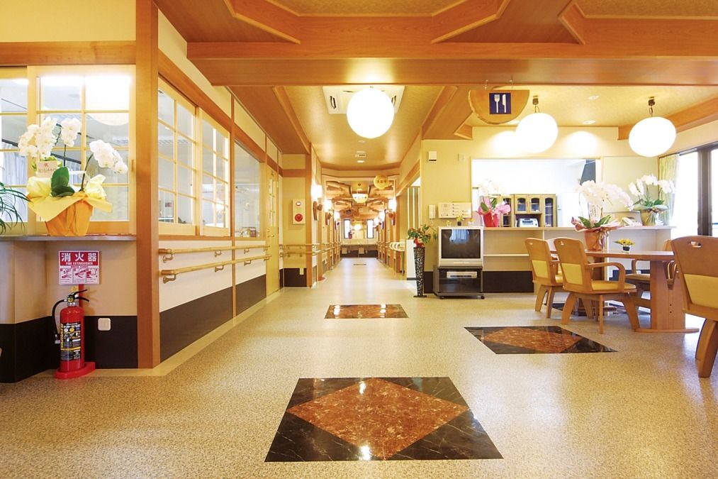 手をたたきながら楽しそうに何かを鑑賞している白髪の高齢女性とピンクのポロシャツを着た若い女性スタッフ。