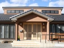 和風の２階建ての建物。瓦屋根が一般の家のような外観。玄関には階段とスロープが設置されている。