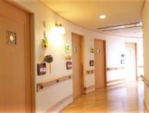 曲線を描く施設内の廊下を写した写真。手すりが取り付けられていて個室のドアが両側に見えている写真
