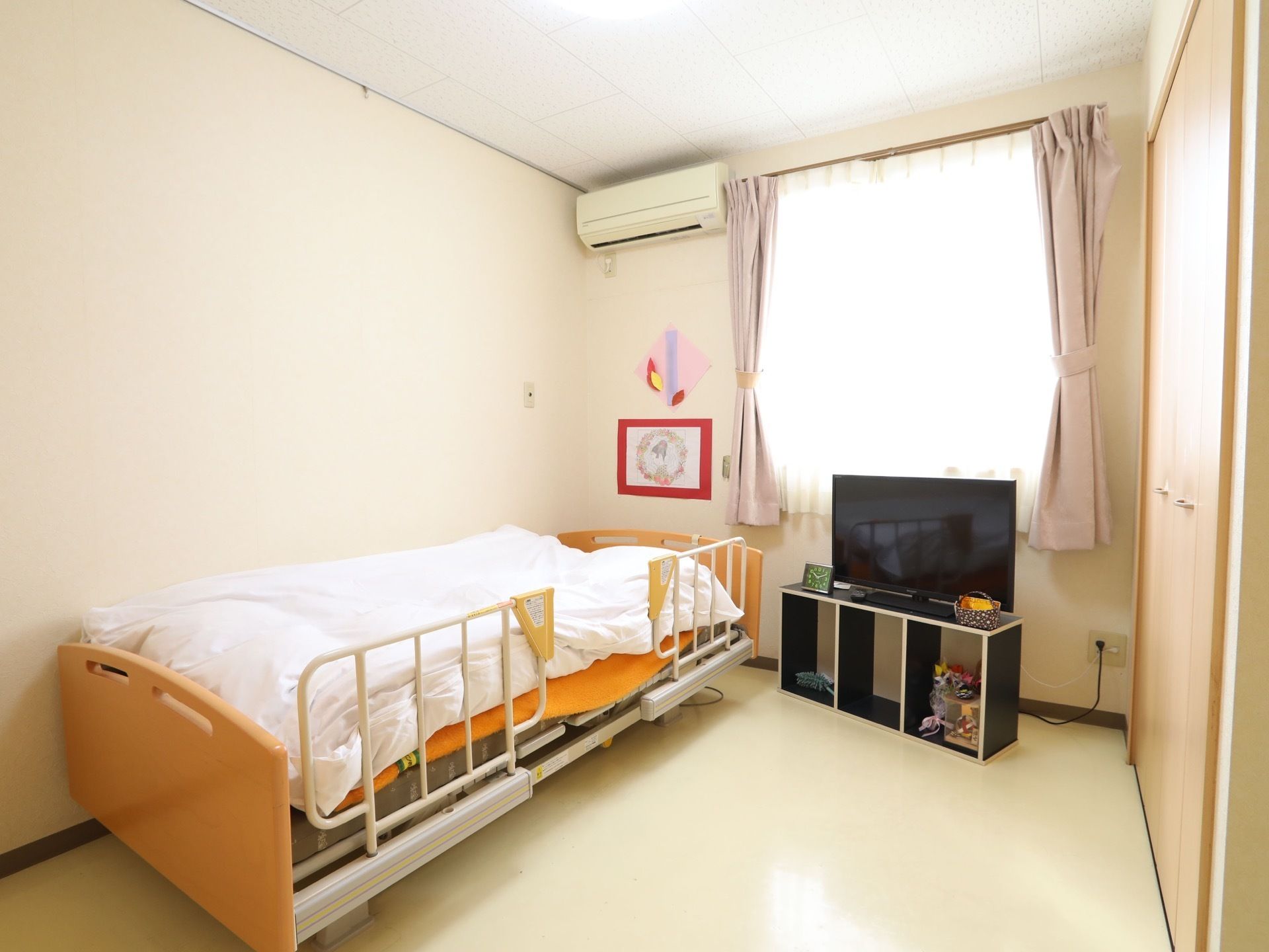 居室は、窓から陽の光がよく入る明るい空間となっている。エアコンやベッド、テレビなどが完備されている。