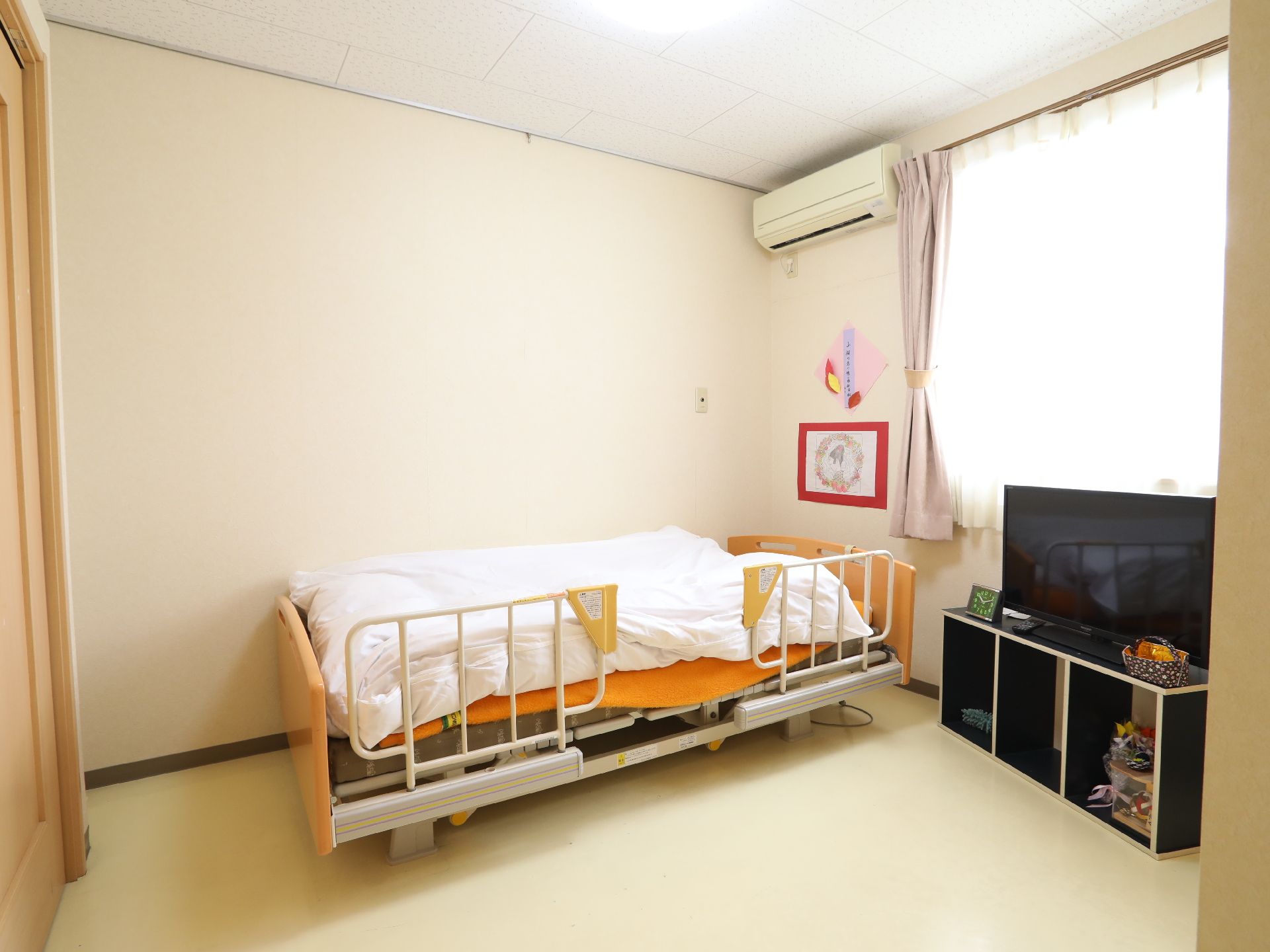 エアコン、手すり付きのベッドとテレビが置かれている居室