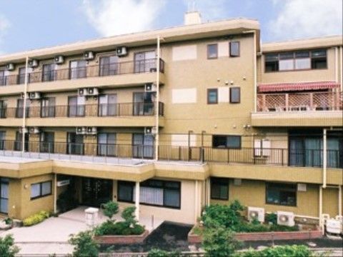 山吹色に近い色調の外壁で、玄関周りに植栽がある施設の外観
