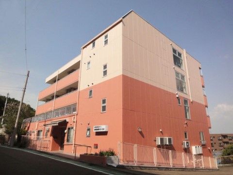 坂になっている道路の横に建つ、ピンク色の外壁が特徴的な４階建ての施設