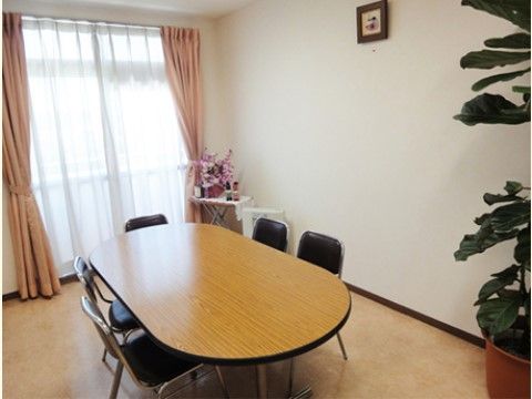談話室の奥には大きな窓があり、ピンク色のカーテンが掛けられている。中央には、5人掛けテーブルが用意されている。