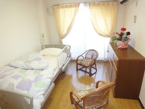 居室は、入居者様が1人で生活するのに十分のスペースが確保されている。室内には横長のタンスがあり、上には花が飾られている。