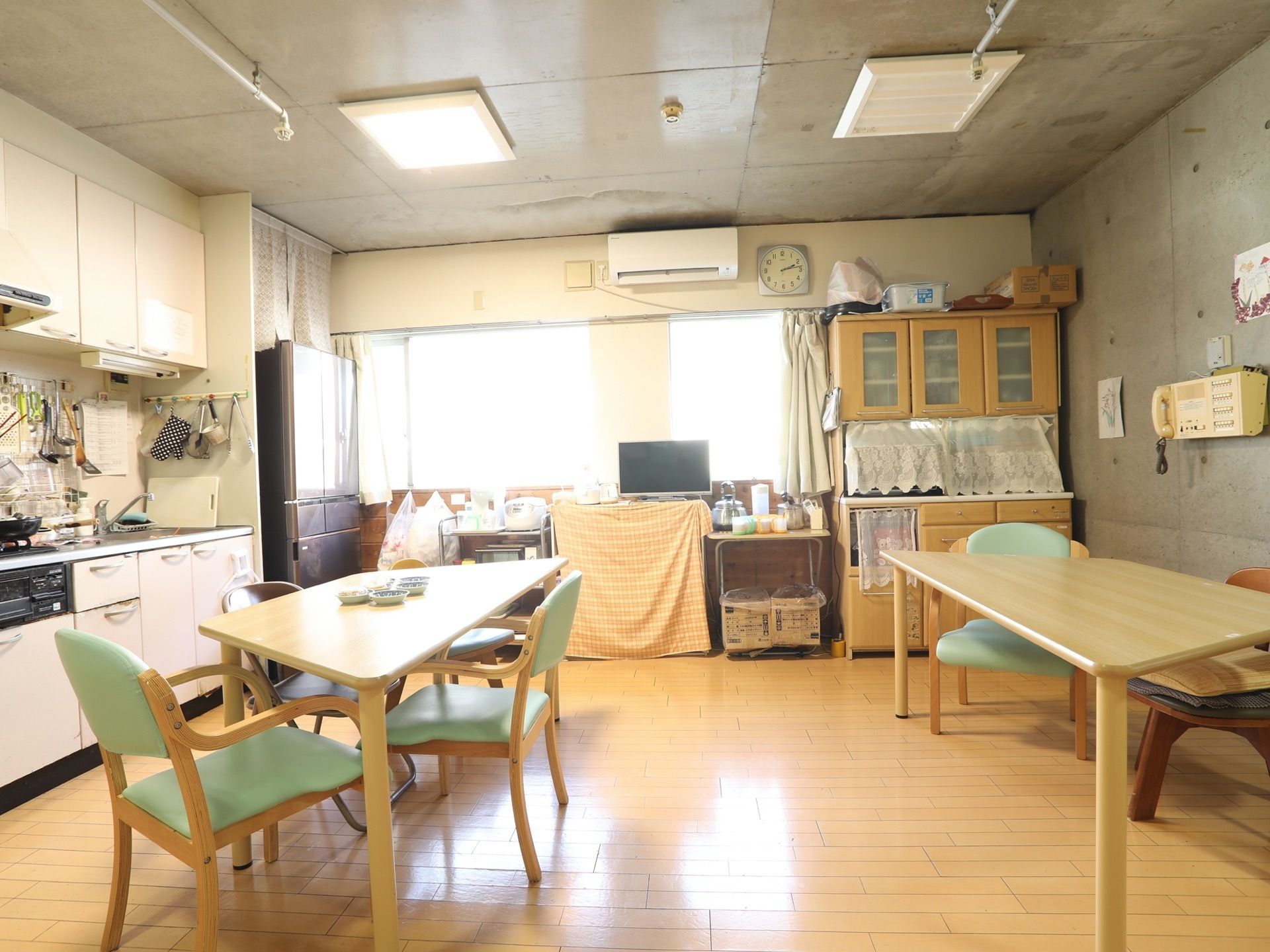 シンクに冷蔵庫、調理器具、食器などがすべて揃った食堂の様子。複数人が座れるテーブルセットが、２つ間隔を空けて配置されている。