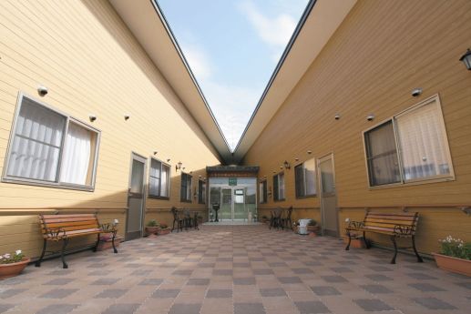 車いすの高齢者と手を握りながら話す介護スタッフの様子。施設内での会話の場面