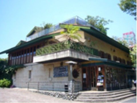 角地に立っている建物で、2階ベランダと屋上には植栽がある。店舗入り口までは階段とスロープの両方がある。