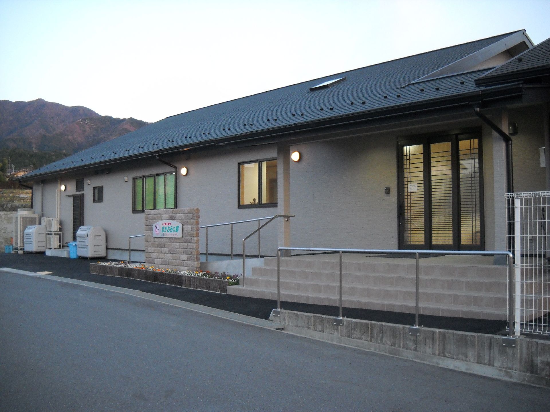 平屋建ての建物には三角の屋根が付き、全体的に茶色っぽい建物。周辺には緑もある。