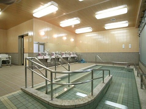 出入り口はスライド式のドアになっている。浴槽にはスロープやステップ、多数の手すりが設けられており安全対策がなされている。