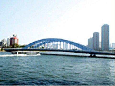 広い空にそびえる高層ビルや雄大な川に浮かぶ水上バスが見える。大きな橋の水色の欄干が弧を描いているのが印象的である。