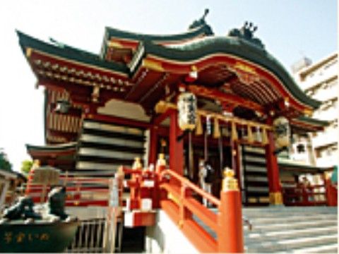階段の下から神社の本殿を見上げている様子。本殿に寄り添うように名物となっている縁起物の像が鎮座している。