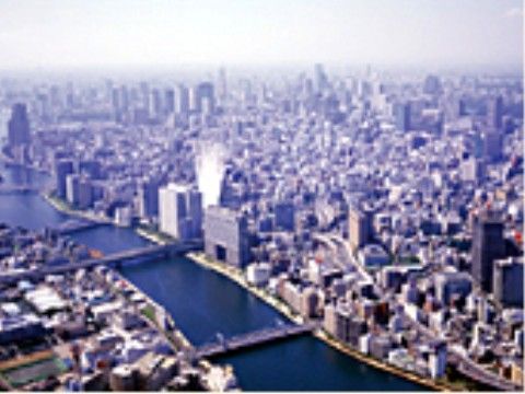 見渡す限りに無数のビルが建ち並ぶ大都会を見下ろす風景。中央を流れる川にはいくつかの橋が架けられている。