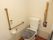 トイレマットと便座カバーが取り付けられている。トイレタンク側とトイレットペーパーフォルダー側に手すりがそれぞれある。