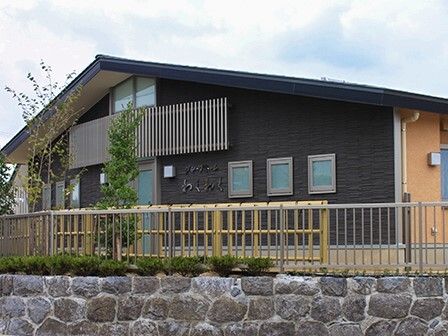 三角屋根が付いた平屋建ての建物は石の塀の上にあり、敷地内には草木が植えられている。