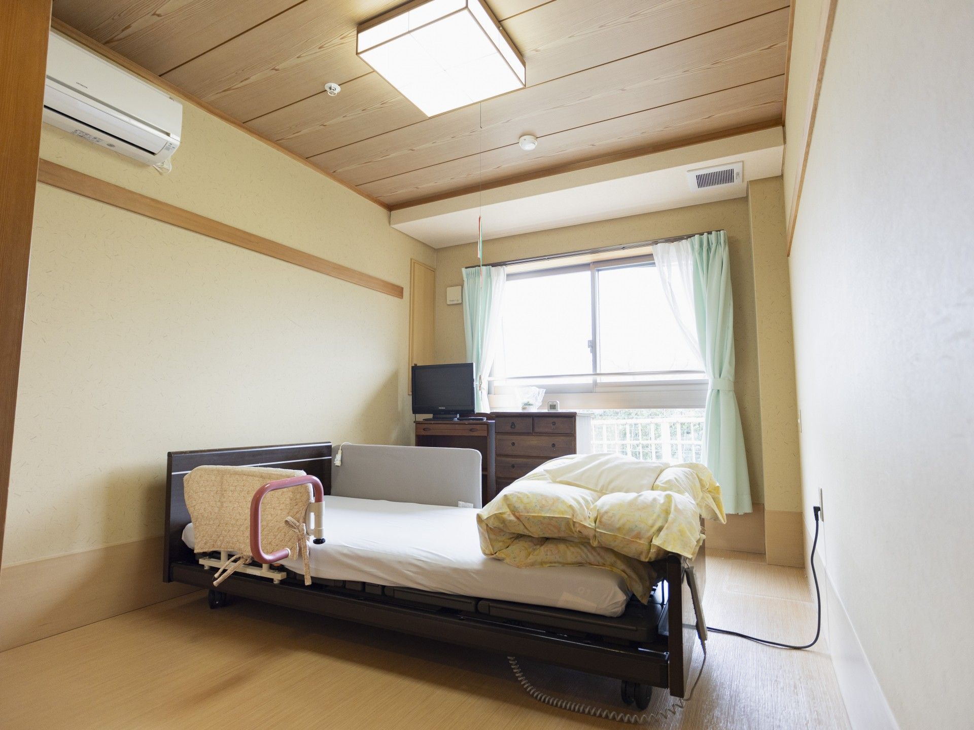 寝具付きのベッドが置かれ、窓にはカーテンが付き、タンスなども並べられている部屋。
