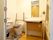 茶色の便座カバーとトイレマットが付けられたトイレの便座部分には上げ下ろし可能な手すりがある。横は洗面台になっている。