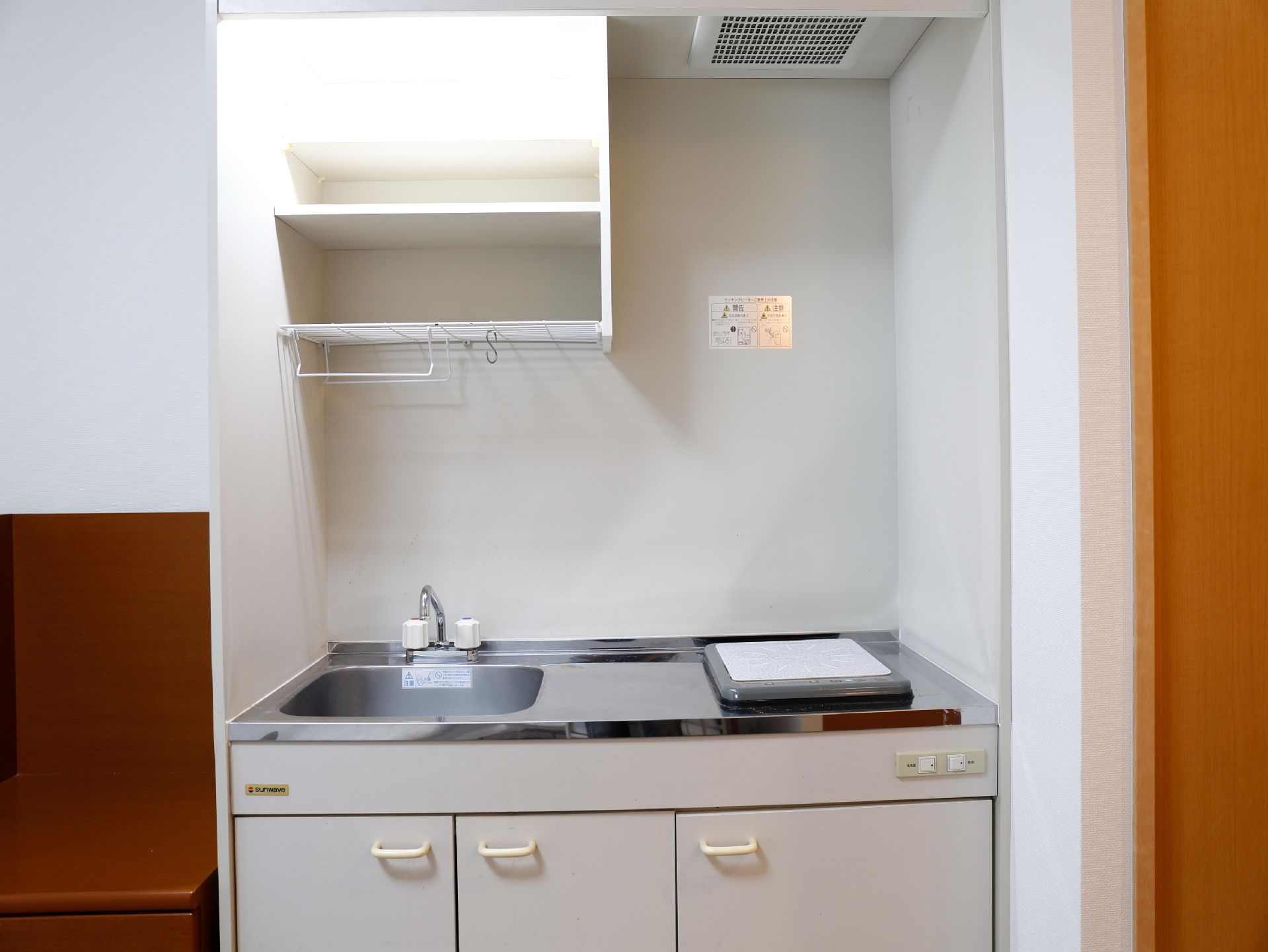 部屋には小さめのキッチンが設置されている。コンロはIHクッキングヒーターになっている。流しの天井には収納棚が付いている。