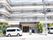 施設は4階建てになっている。施設入口近くには車やバイクが止められている。植え込みには木が植えられている。