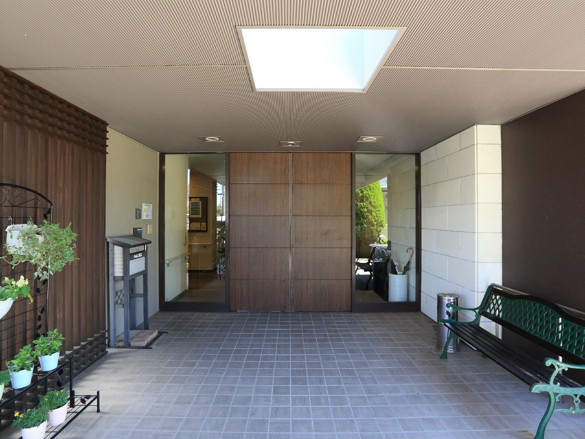 重厚な雰囲気のある施設の入り口。手入れの行き届いたプランタがあり、ベンチが外に設置されている。屋根があり、雨に濡れることはない。