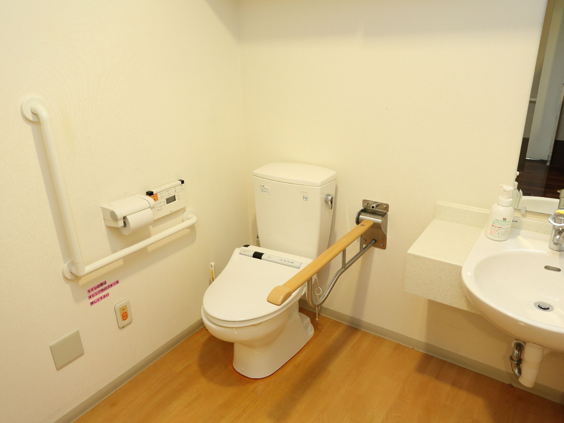 トイレはは白い壁とフローリングの床になっていて清潔感がある。立ったり座ったりする時に便利な手すりが両側についている。