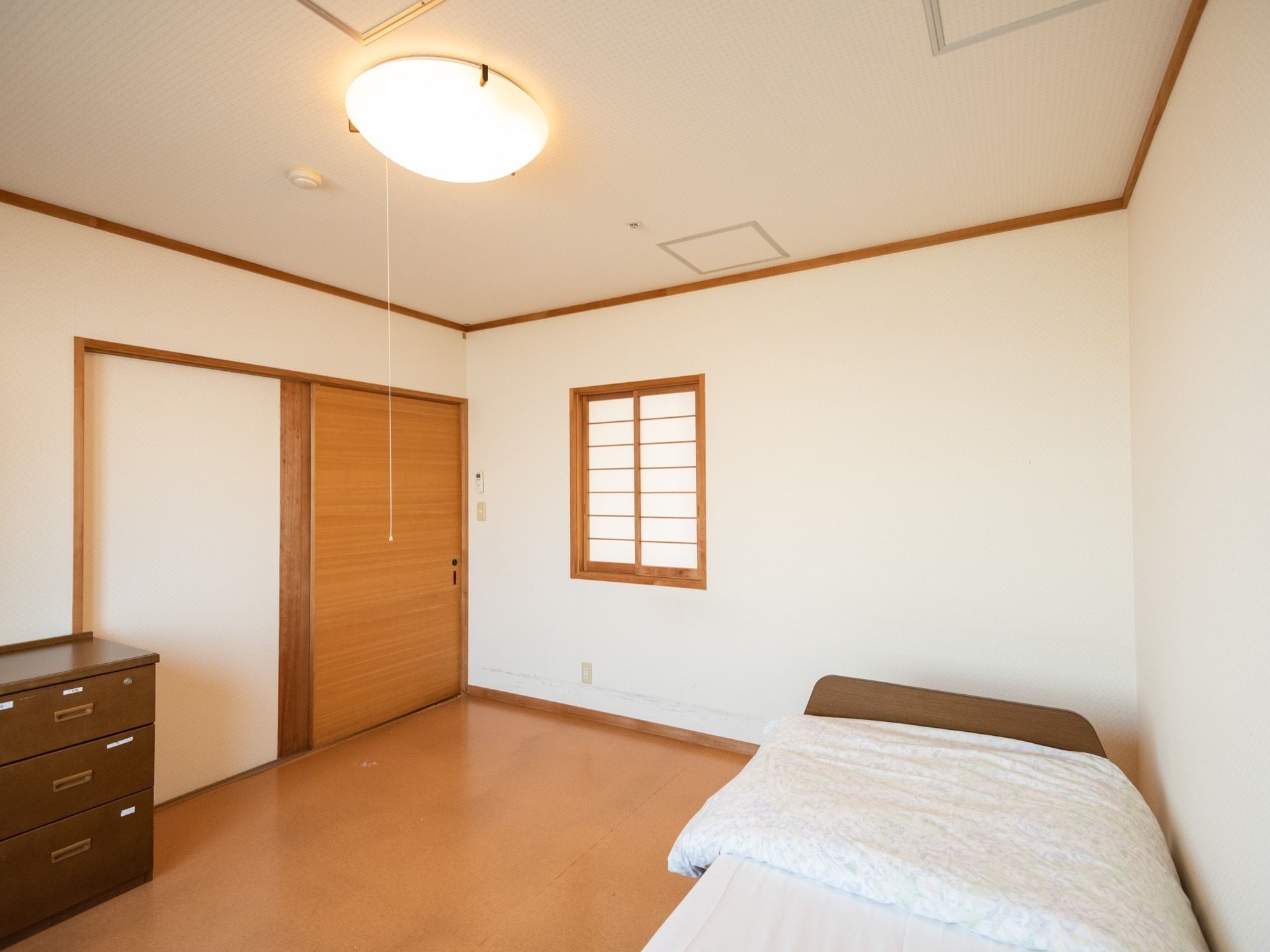 個室の部屋にベッドが設置されており、寝具が用意されている。収納棚が置かれている。扉はスライドドアである。