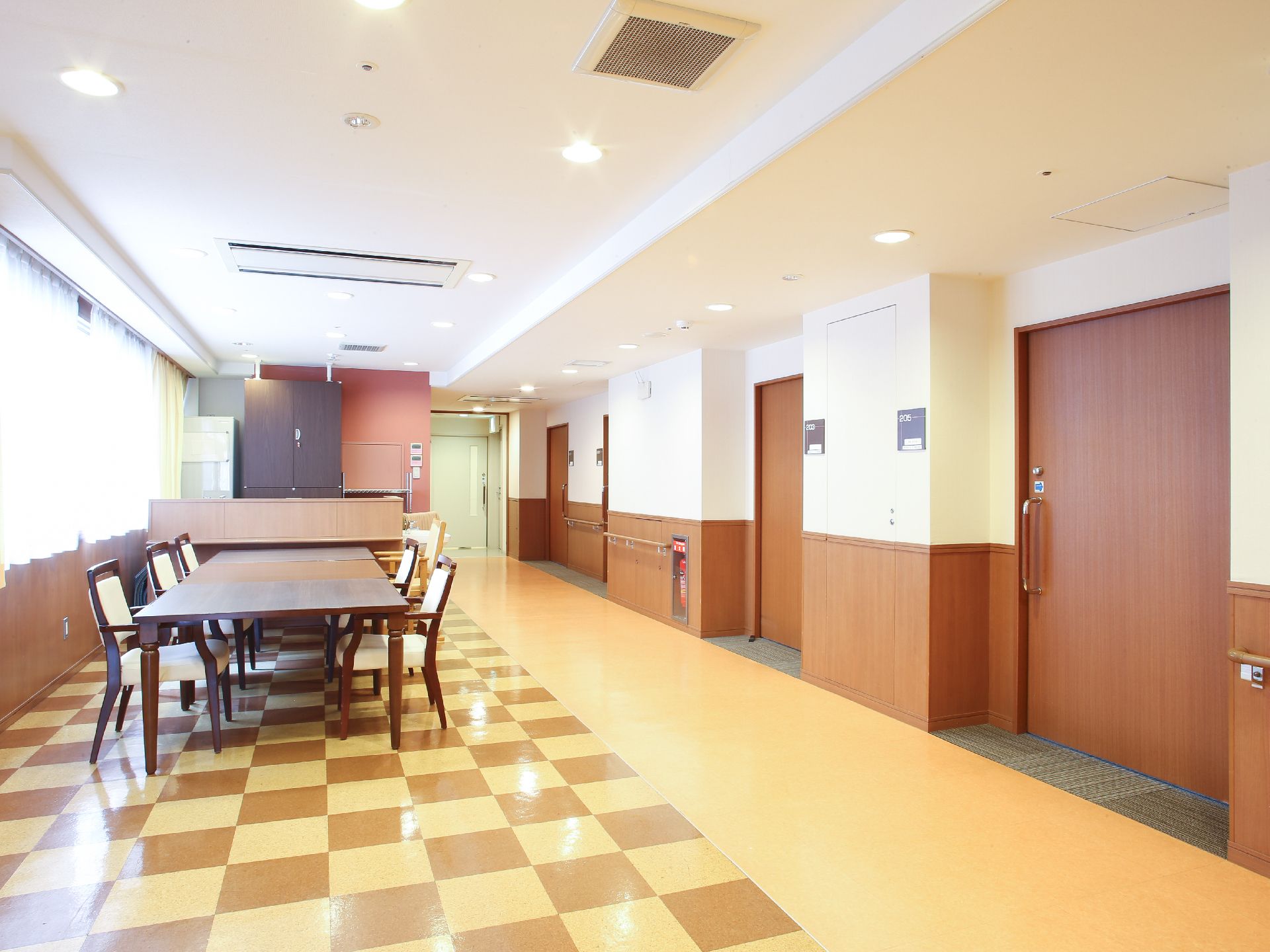 部屋には大きな窓がある。部屋の扉、壁側には手すりが取り付けられている。机3台と椅子6脚が並べられている。