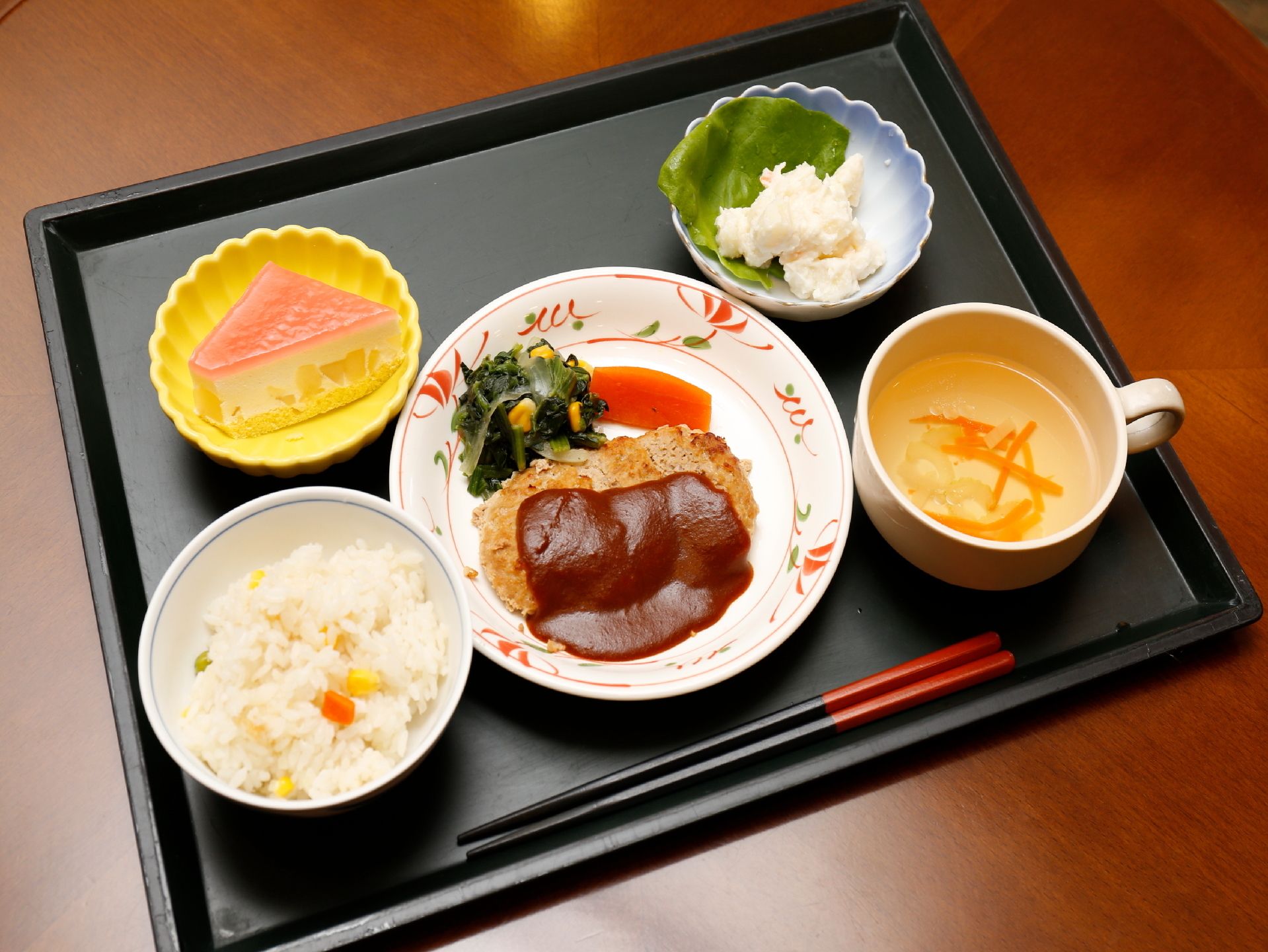 炊き込みピラフ、ハンバーグ、サラダ、スープ、デザートがついた食事。栄養バランスから彩りまで考えられて食欲をそそるメニュー。