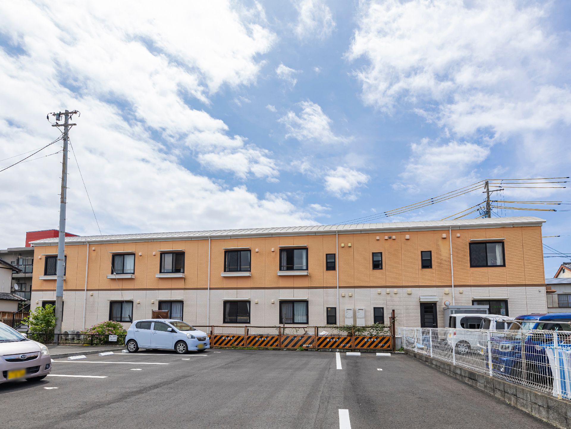 緑の多い屋外で散策を楽しんでいる眼鏡姿の高齢男性とピンクのエプロンを付けた女性スタッフ。男性は車いすに座っている。