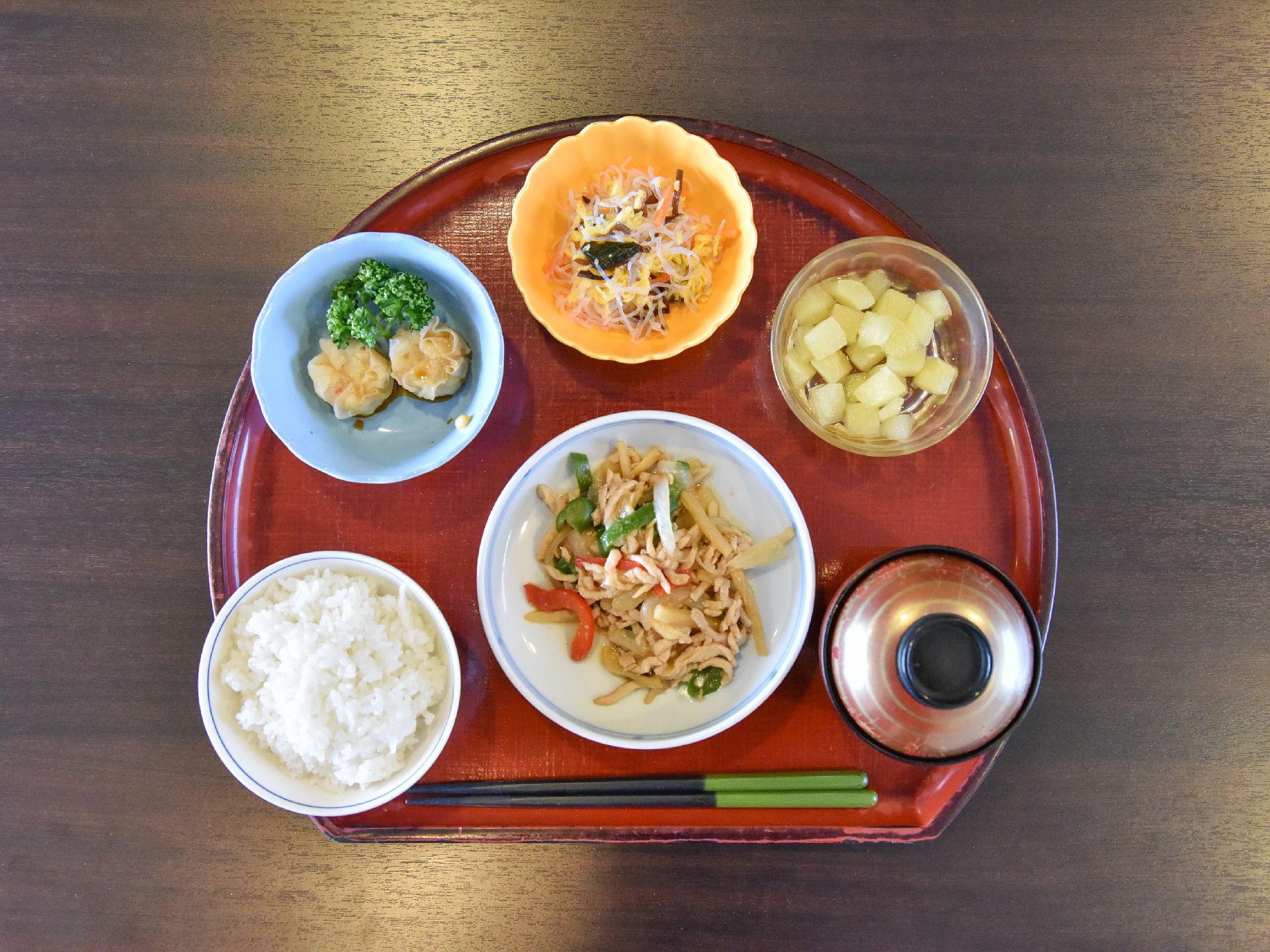 炒め物、シュウマイ、中華風サラダ、デザートが朱色のお盆に並べられている。栄養バランスを考えた食欲をそそるメニューが配膳されている。