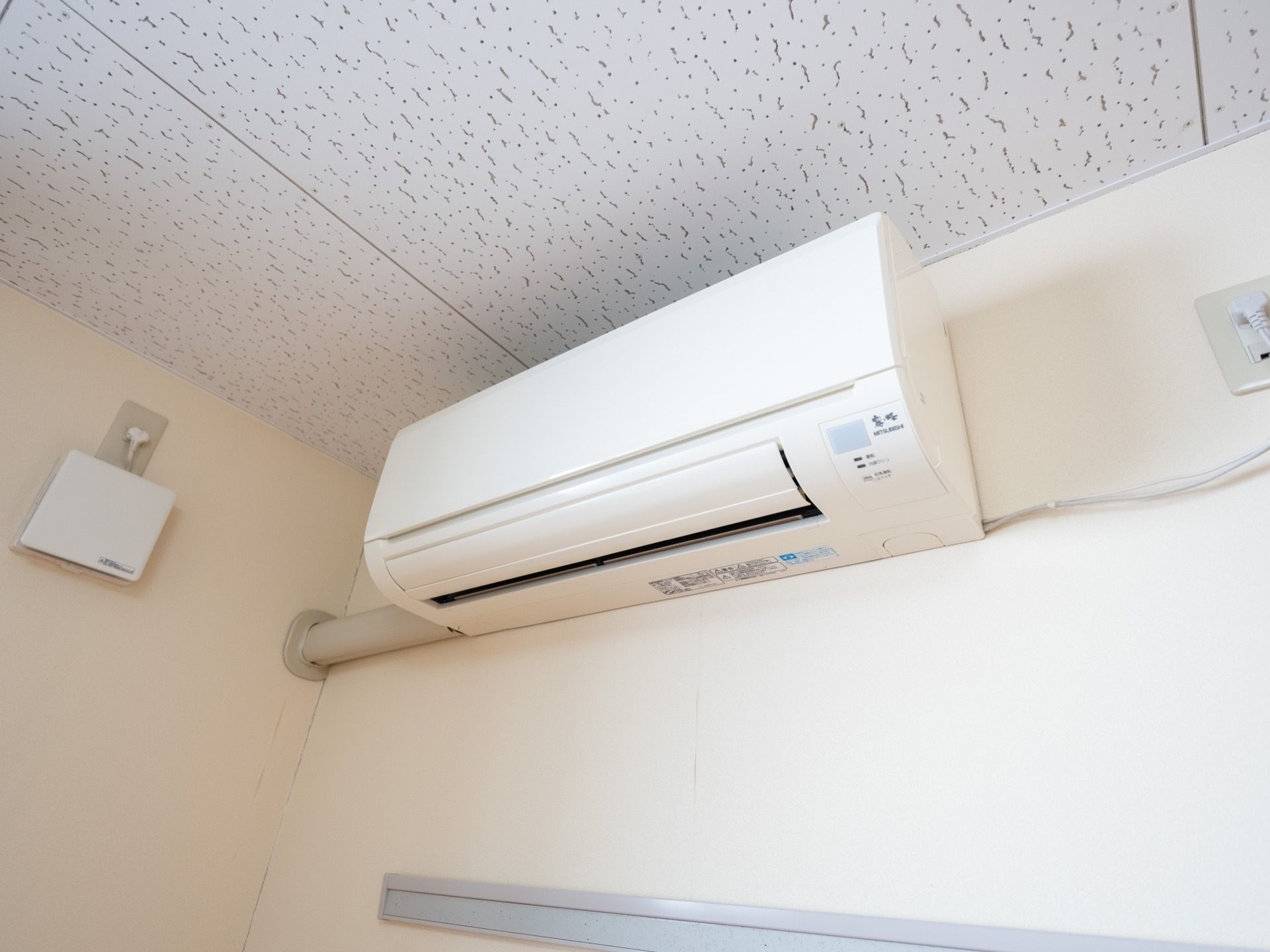 個室の部屋である。壁と天井は清潔感のある白で統一されている。エアコンが設置されており、換気口が設けられている。