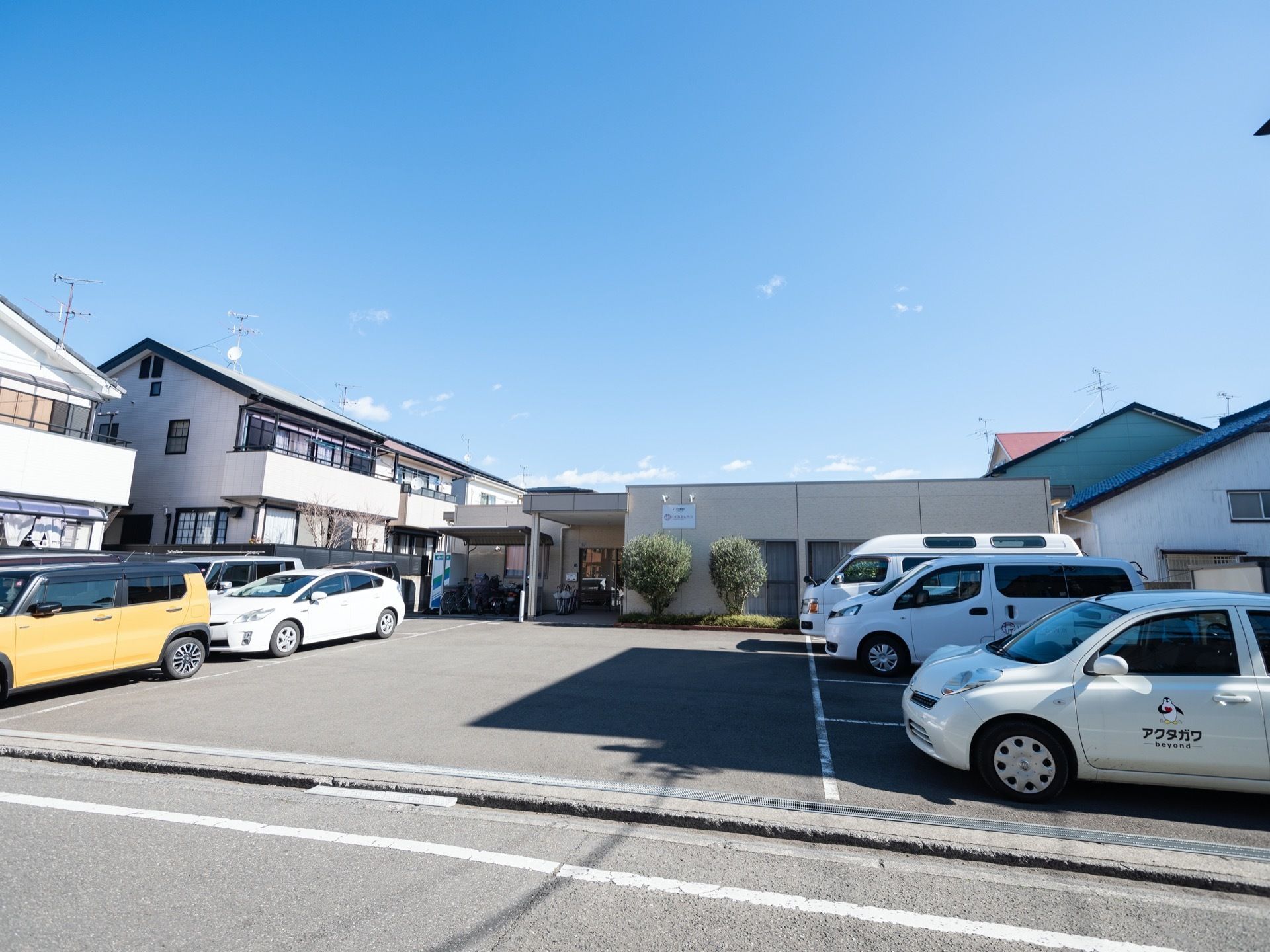 家庭的な雰囲気の施設外観である。平屋建ての建物になっており、敷地内には駐車場が設けられている。車が何台か停められている。