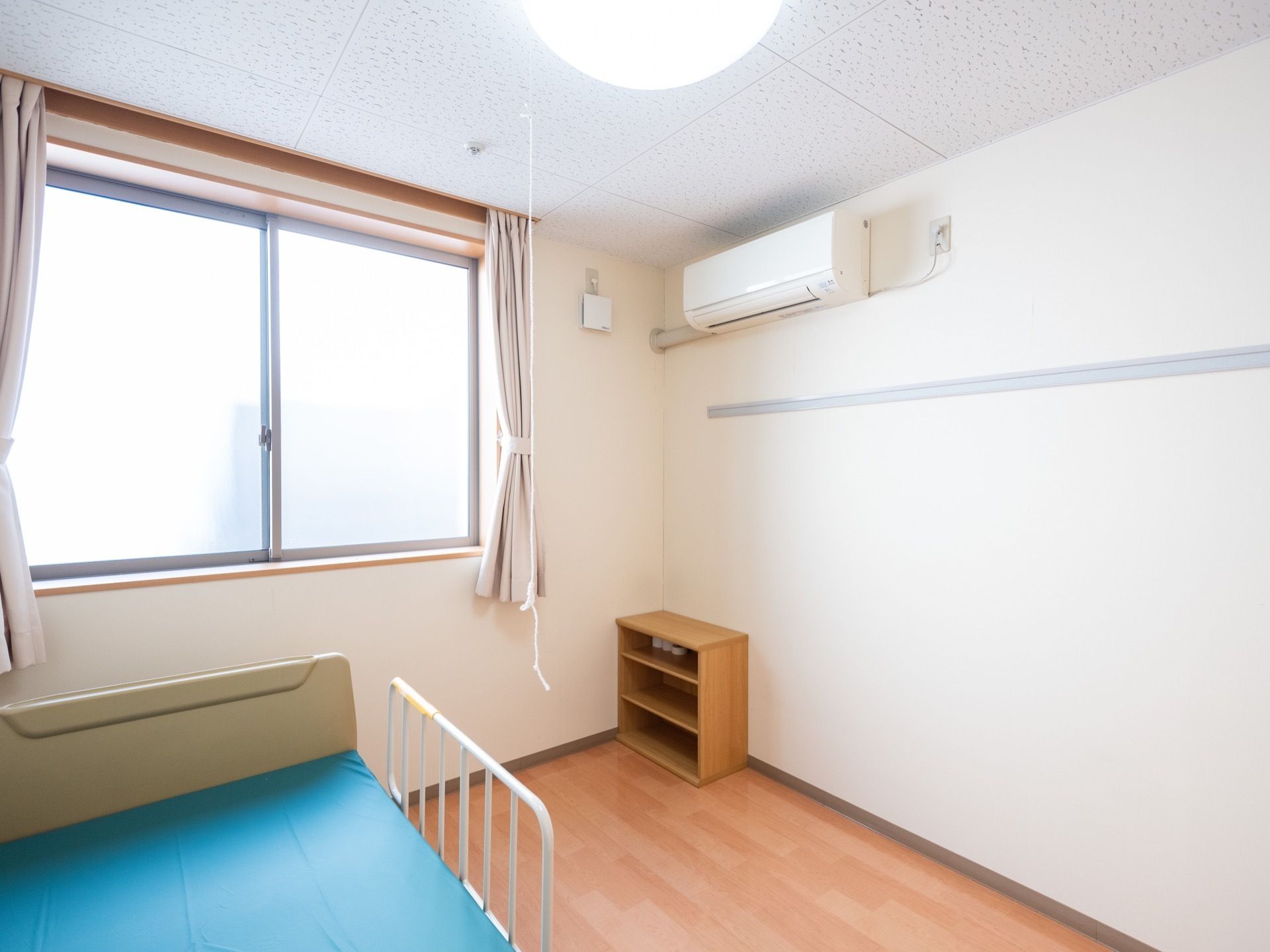 窓からは自然光が差し込み、明るい。カーテンが掛けられている。ベッドが用意されており、収納のカラーボックスが備わっている。