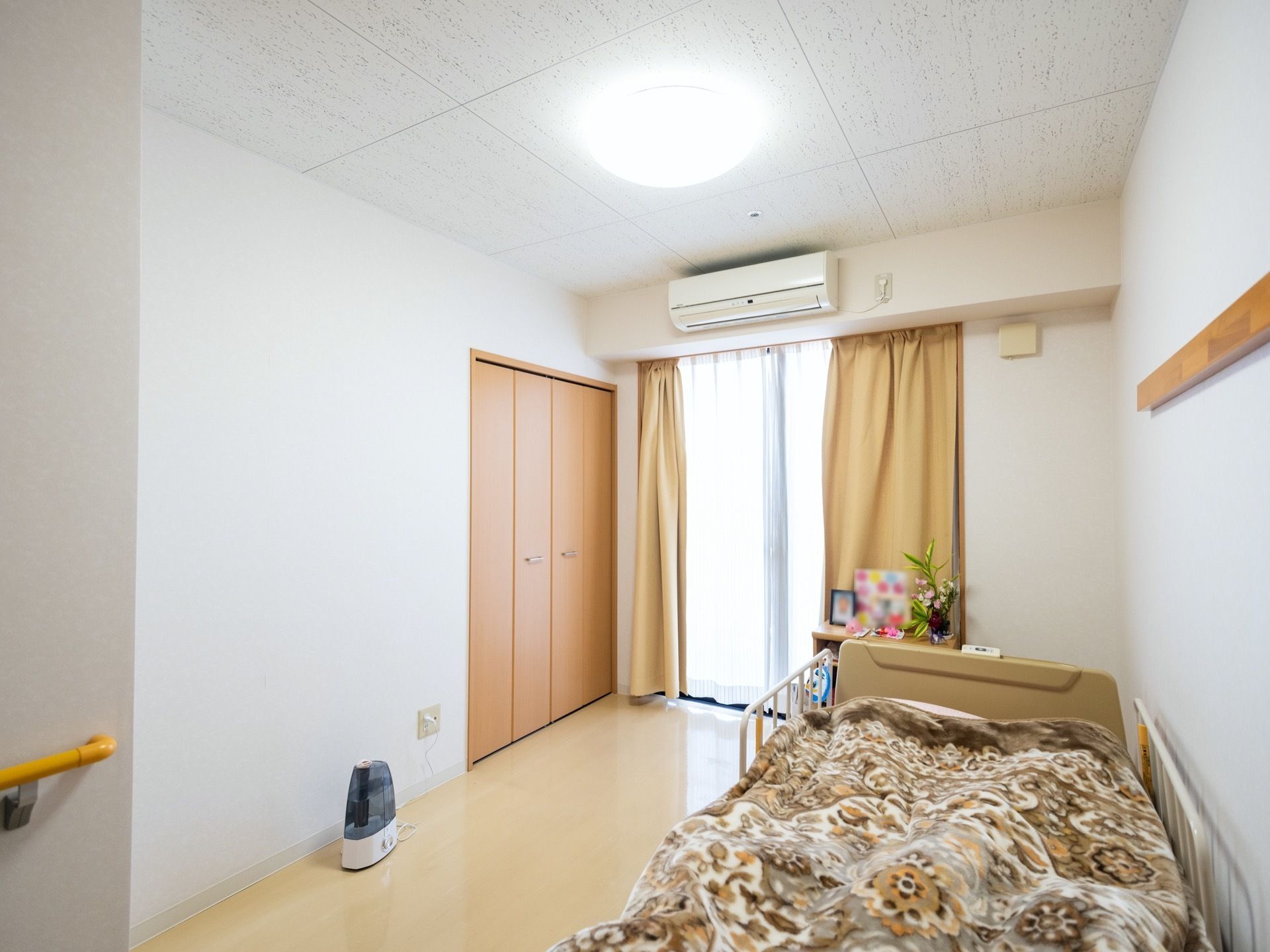 ワンルームタイプの個室である。ベッドが用意されており、布団が備わっている。窓にはカーテンが掛けられている。
