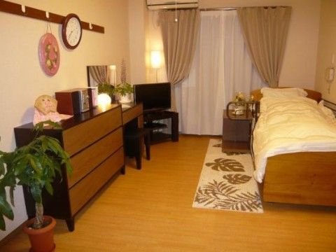テレビやエアコン、収納棚など一通りのものが揃っている部屋。ベッドの横に小さな棚があり、その下にカーペットが敷かれている。