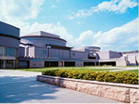 広い敷地に建っている建物の前が広場になっている。外壁は淡い色合いで、階上の中央が丸いドーム型にデザインされている。