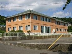 オレンジの外壁の２階建ての建物の周辺には緑が多い。