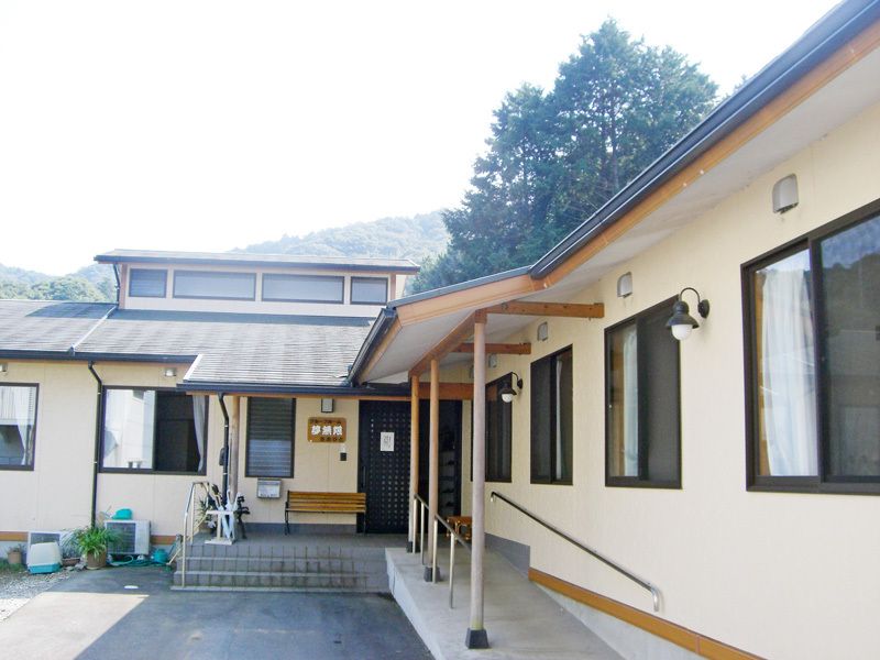和風の平屋建ての建物。周辺には自然が残り、アットホームな雰囲気。玄関前にはベンチが置かれている。