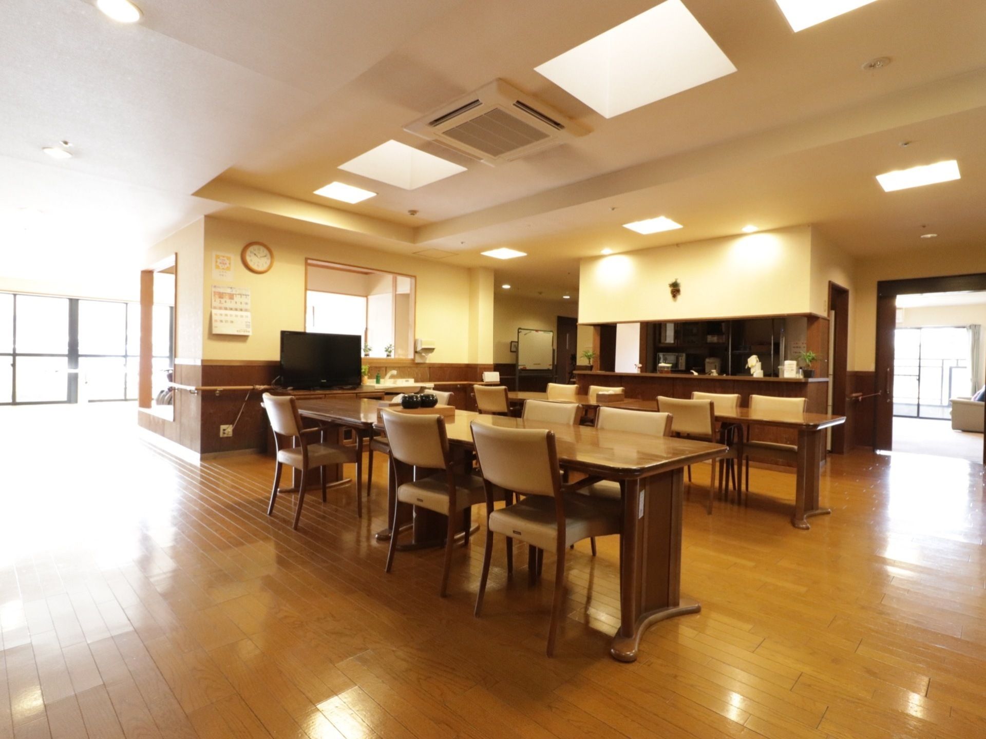 明るく広い食堂。壁側にはテレビを設置している。天井にはエアコンがある。奥にはキッチンのカウンターがある。