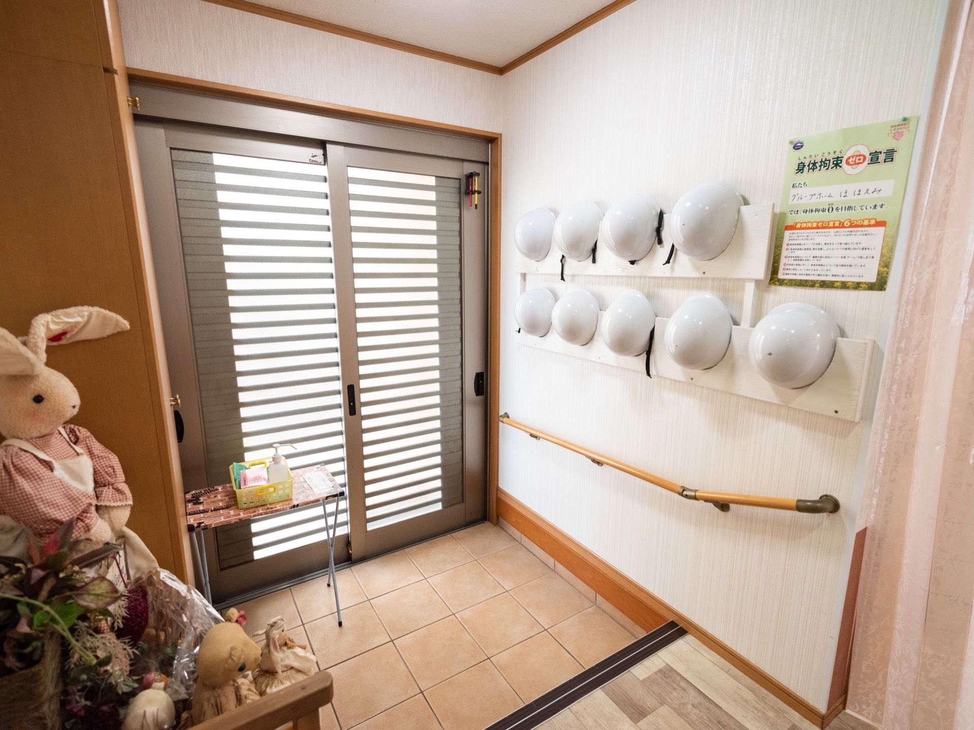 ドアのガラスから光が差し込む明るい玄関。うさぎのぬいぐるみが癒しを与える。壁にはヘルメットが多数用意されている。