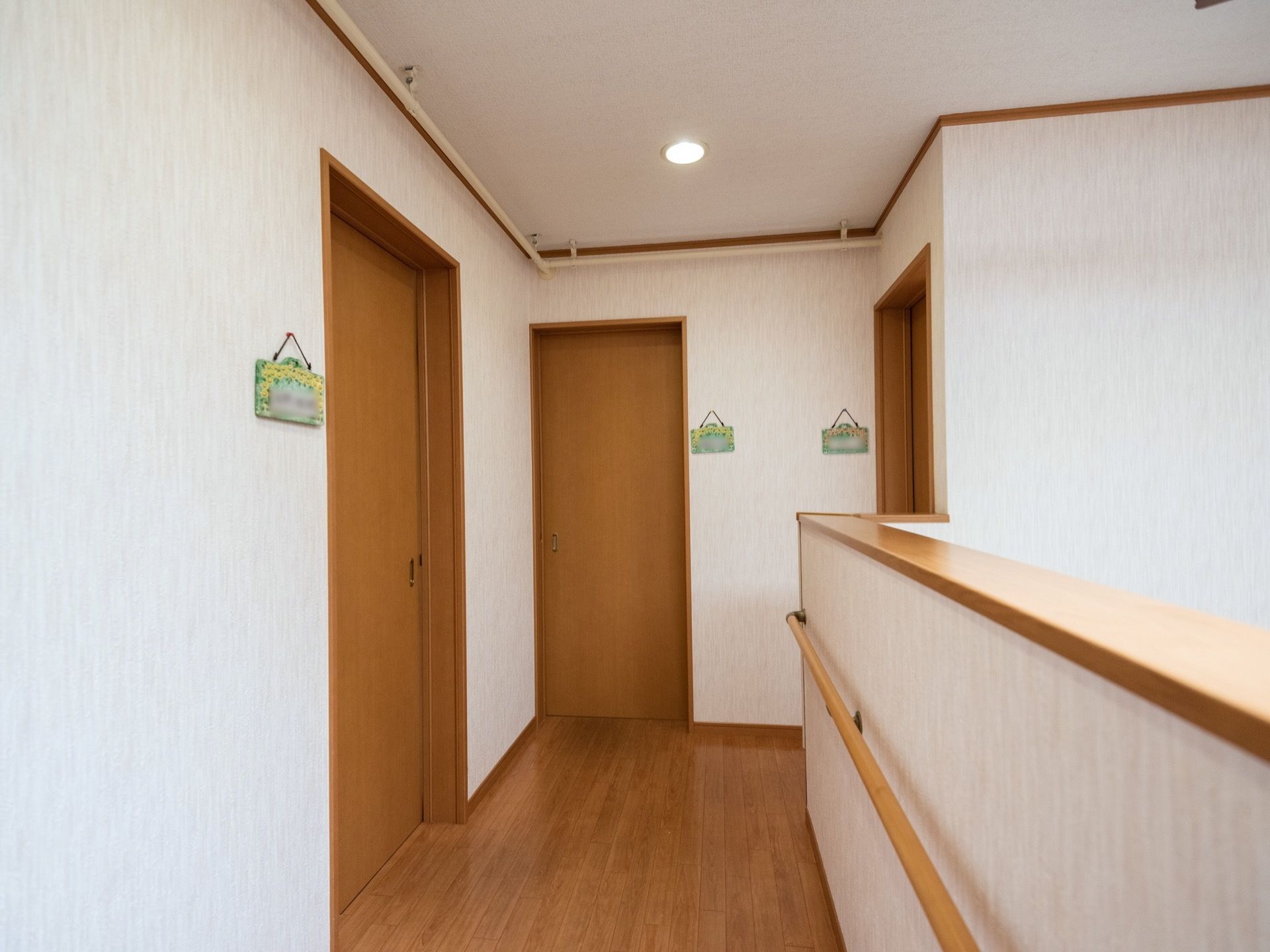 白い壁が清潔感をかもし出している２階部分の通路である。居室が３部屋あり、手作りの表札がかかっている。