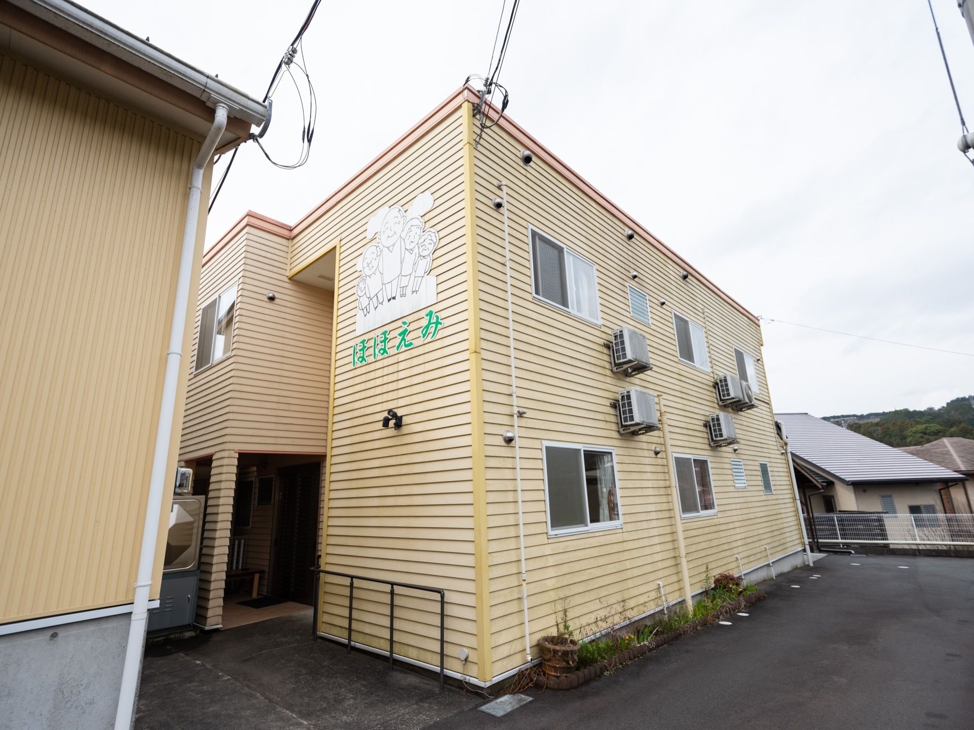 淡いオレンジで統一された２階建ての建物である。周辺はアスファルトで整地されており、フェンスが設置されている。