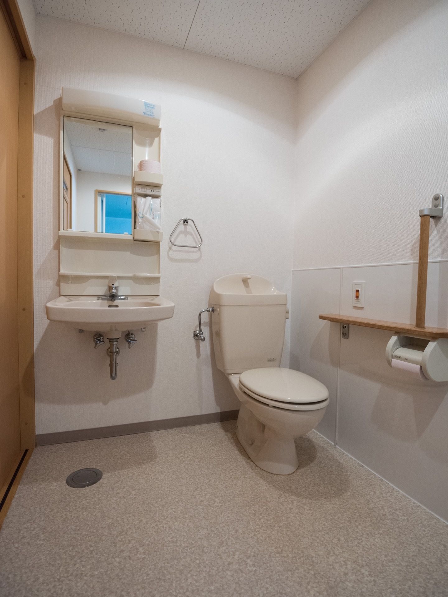 トイレと洗面化粧台が同スペースに設置されている。白ベースに木目調の建具でまとめ、床には何も置かず、スッキリとした空間である。