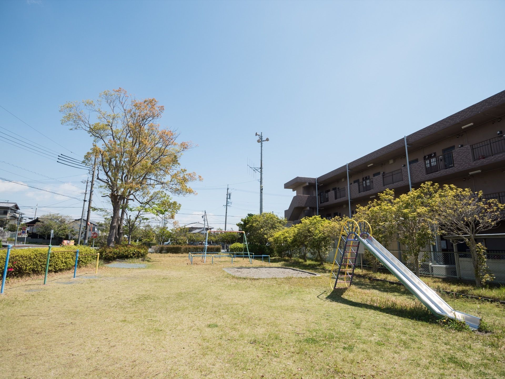 施設の横にある公園である。砂場やブランコ、滑り台、鉄棒が設置されている。木や草が生え、緑豊かな環境である。