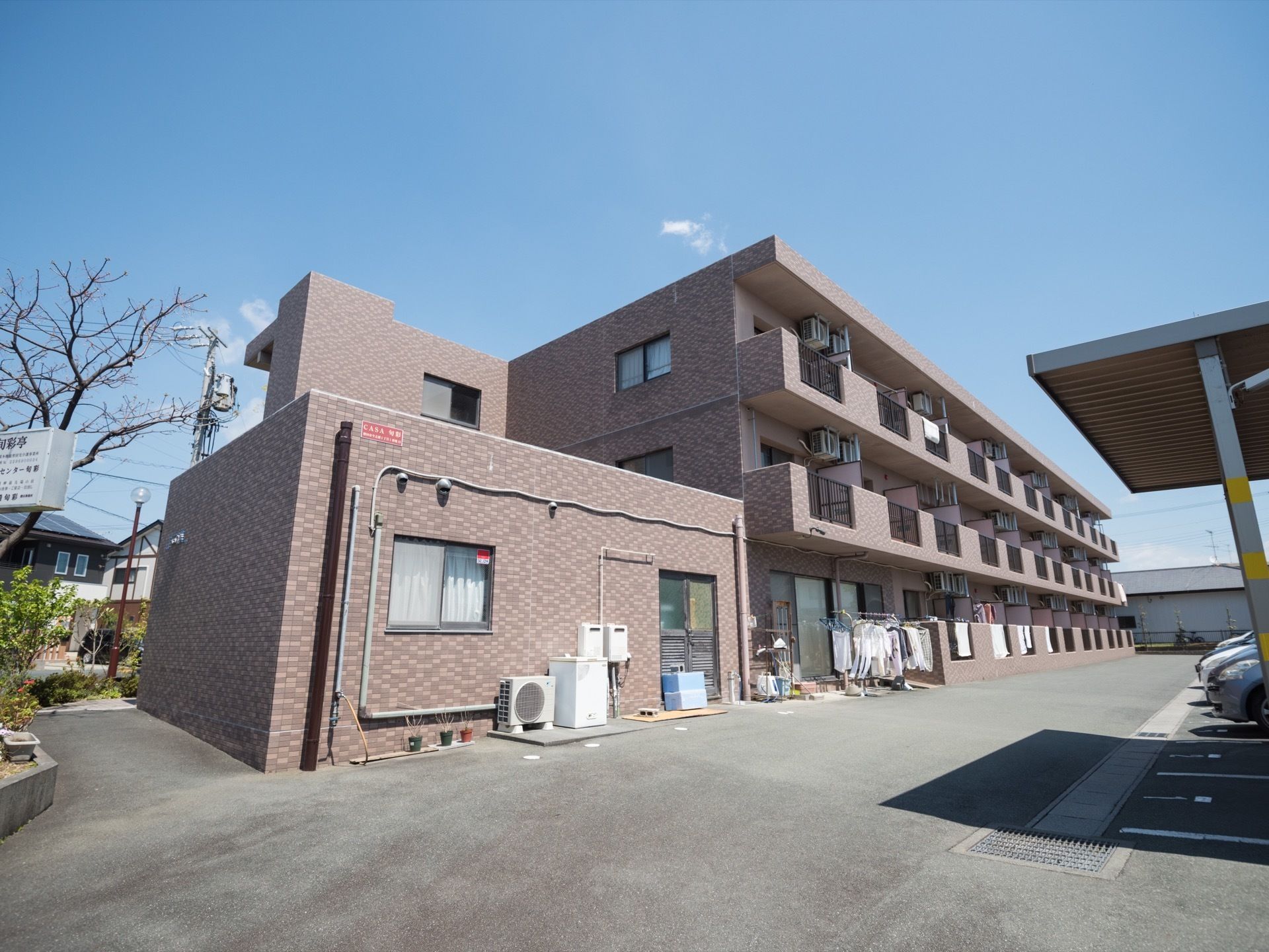 レンガ調の落ち着いた色合いで、頑丈な造りであることが伺える３階建ての施設建物である。ベランダ側に駐車スペースを設けている。