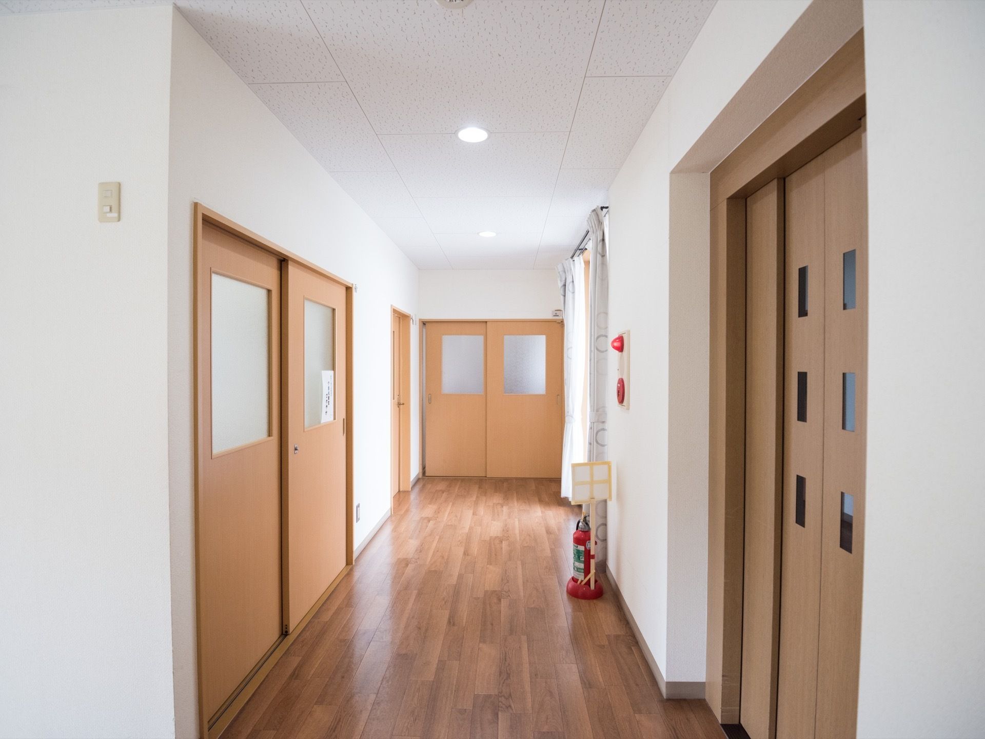 木目調の床、白色の壁に造られた通路である。幅が広々としている。壁側に消火器や火災報知器も備え付けられている。